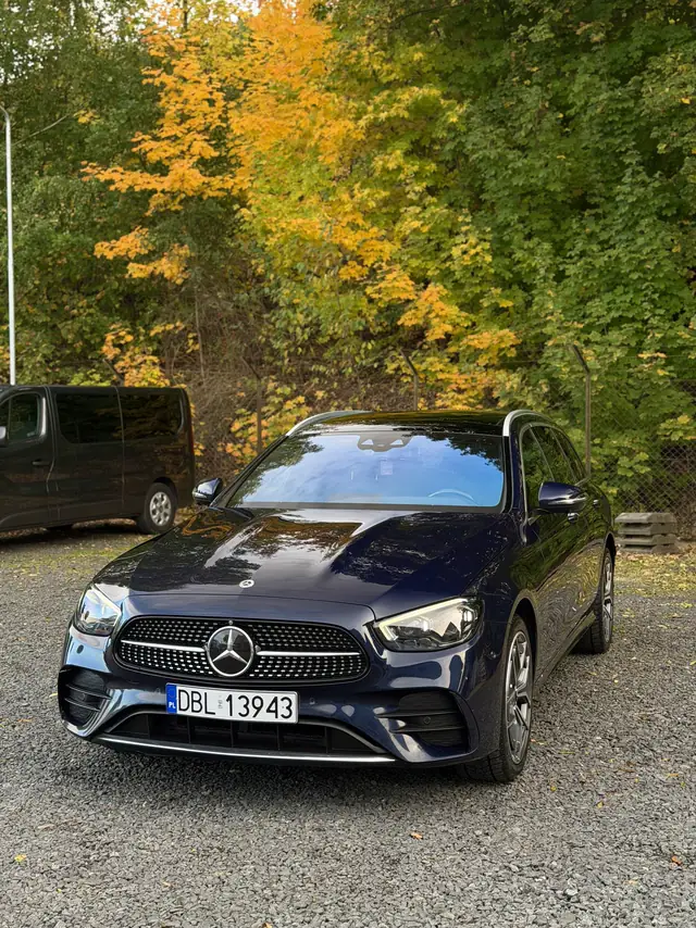 Granatowy Mercedes E-Class kombi na tle jesiennych drzew, lakier odbija korony drzew